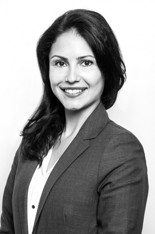 Junge Frau lächelt für ein Bewerbungsfoto in die Kamera vor hellem Hintergrund