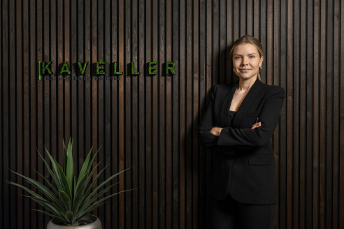 Mitarbeiterin vor einer Holzwand mit Firmenlogo