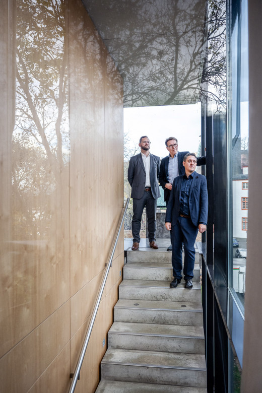 Gruppenfoto von 3 Geschäftsführern durch eine Glaswand mit Spiegelung