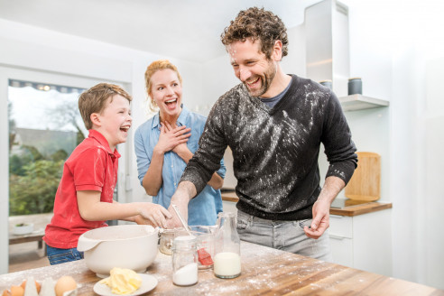 Eltern backen mit Sohn in der Küche und lachen.