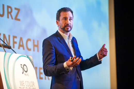 Redner auf einer Bühne vor dem Firmenlogo